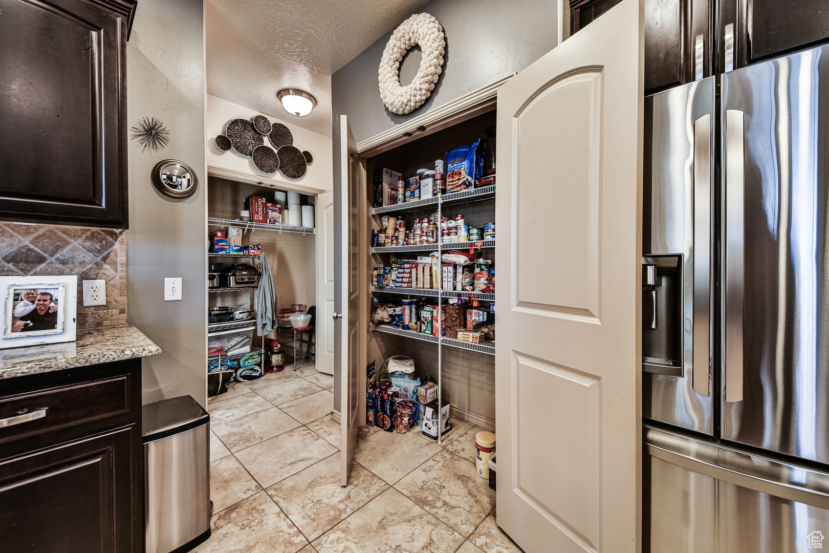 Kitchen with dark brown cabinetry, stainless steel refrigerator with ice dispenser, and tasteful backsplash