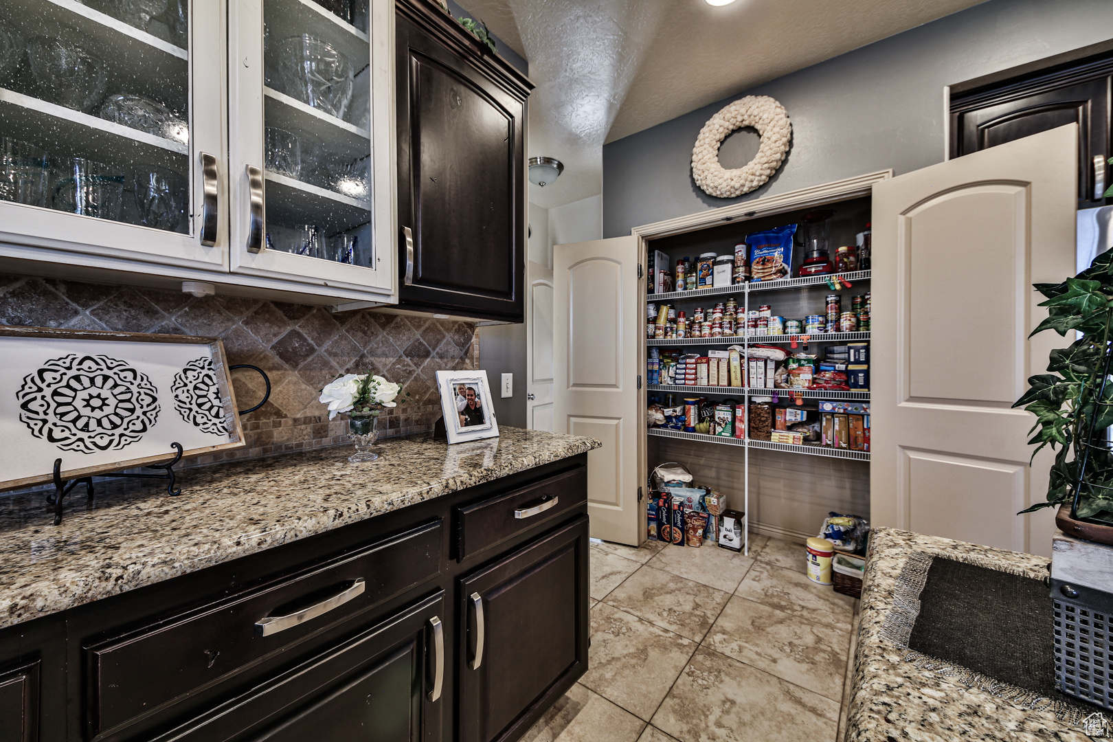 Kitchen with tasteful backsplash, light stone countertops, dark brown cabinets, and light tile flooring