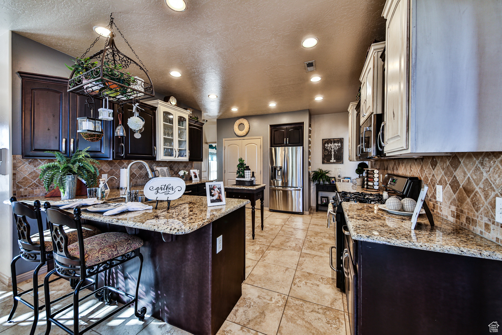 Kitchen with stainless steel fridge with ice dispenser, light tile flooring, backsplash, and light stone countertops