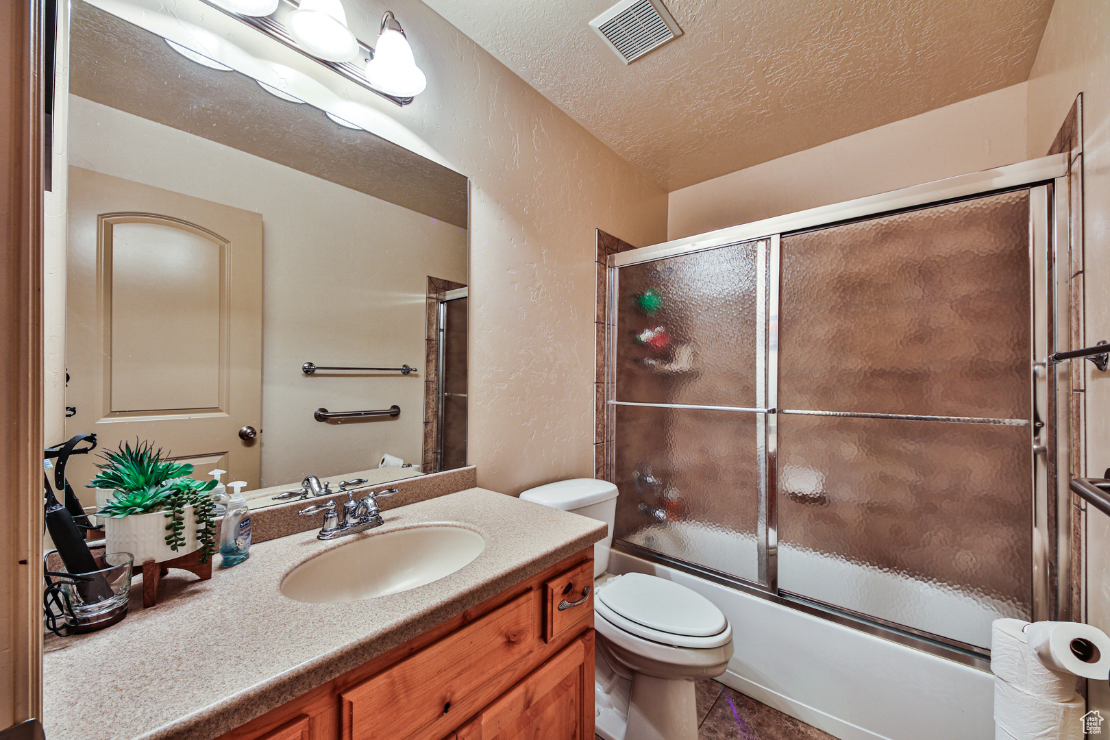 Full bathroom with enclosed tub / shower combo, oversized vanity, tile flooring, toilet, and a textured ceiling