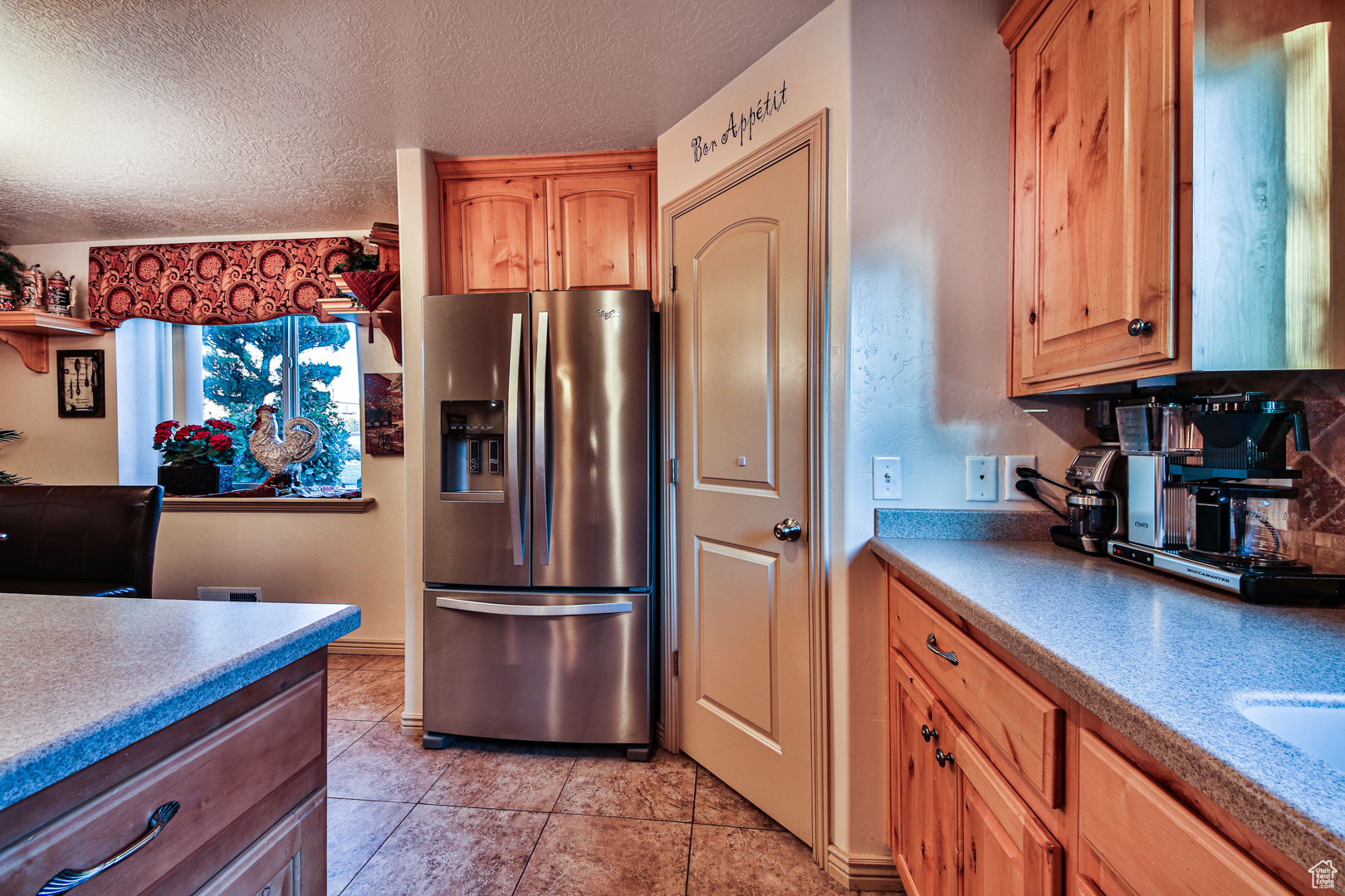Kitchen featuring backsplash, a textured ceiling, light tile flooring, and stainless steel fridge