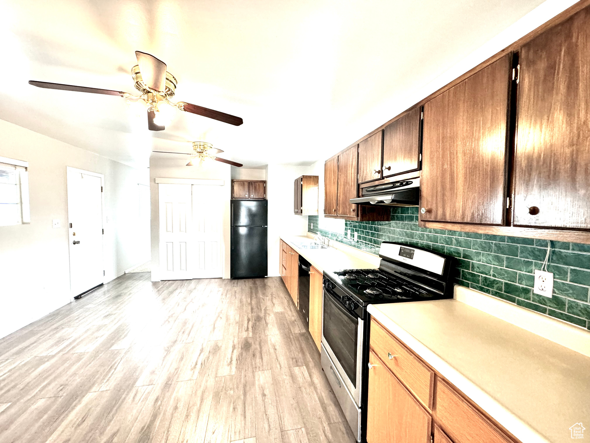 Kitchen featuring ceiling fan, sink, backsplash, black appliances, and light hardwood / wood-style flooring