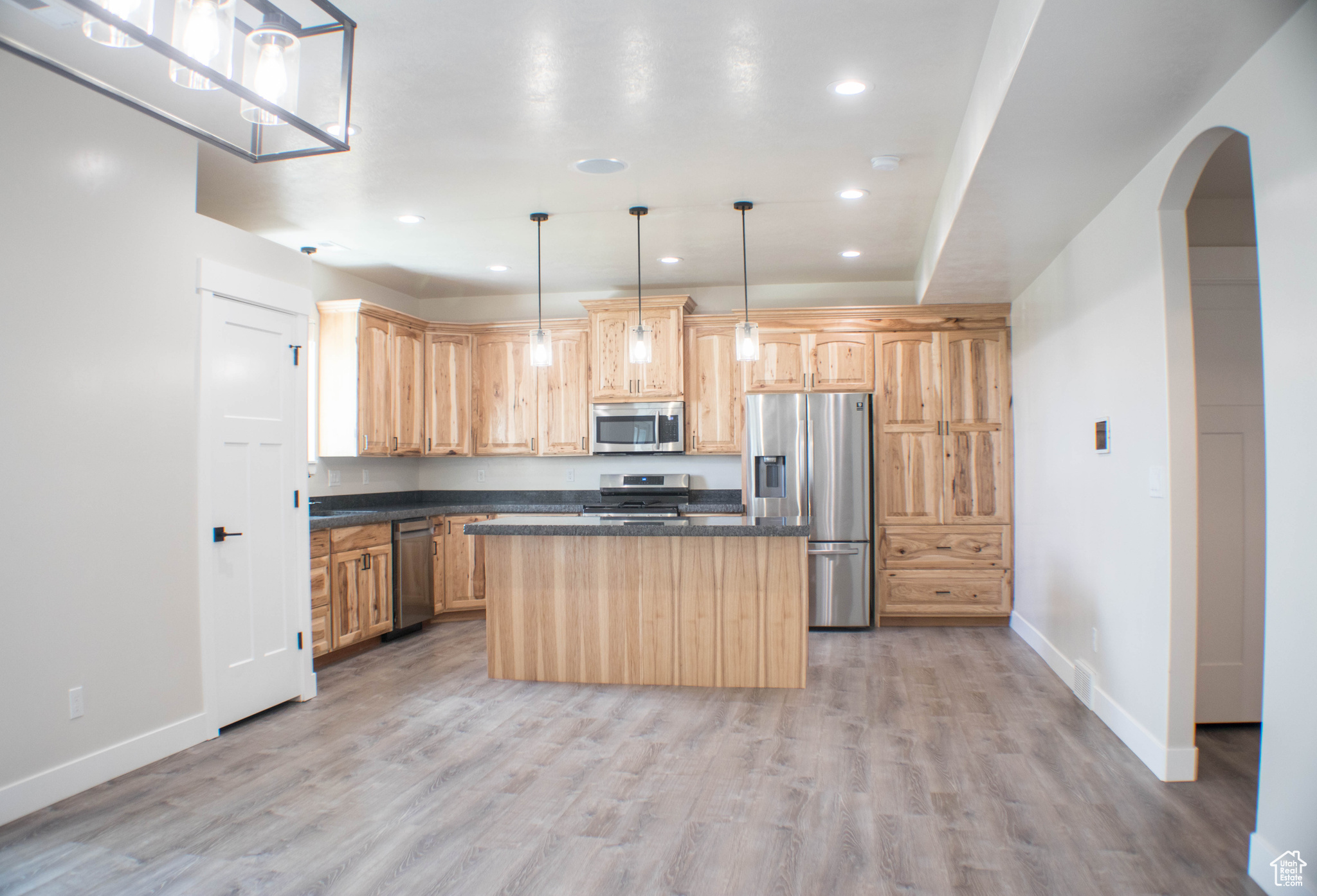 Kitchen with appliances with stainless steel finishes, a kitchen island, light hardwood / wood-style floors, and hanging light fixtures