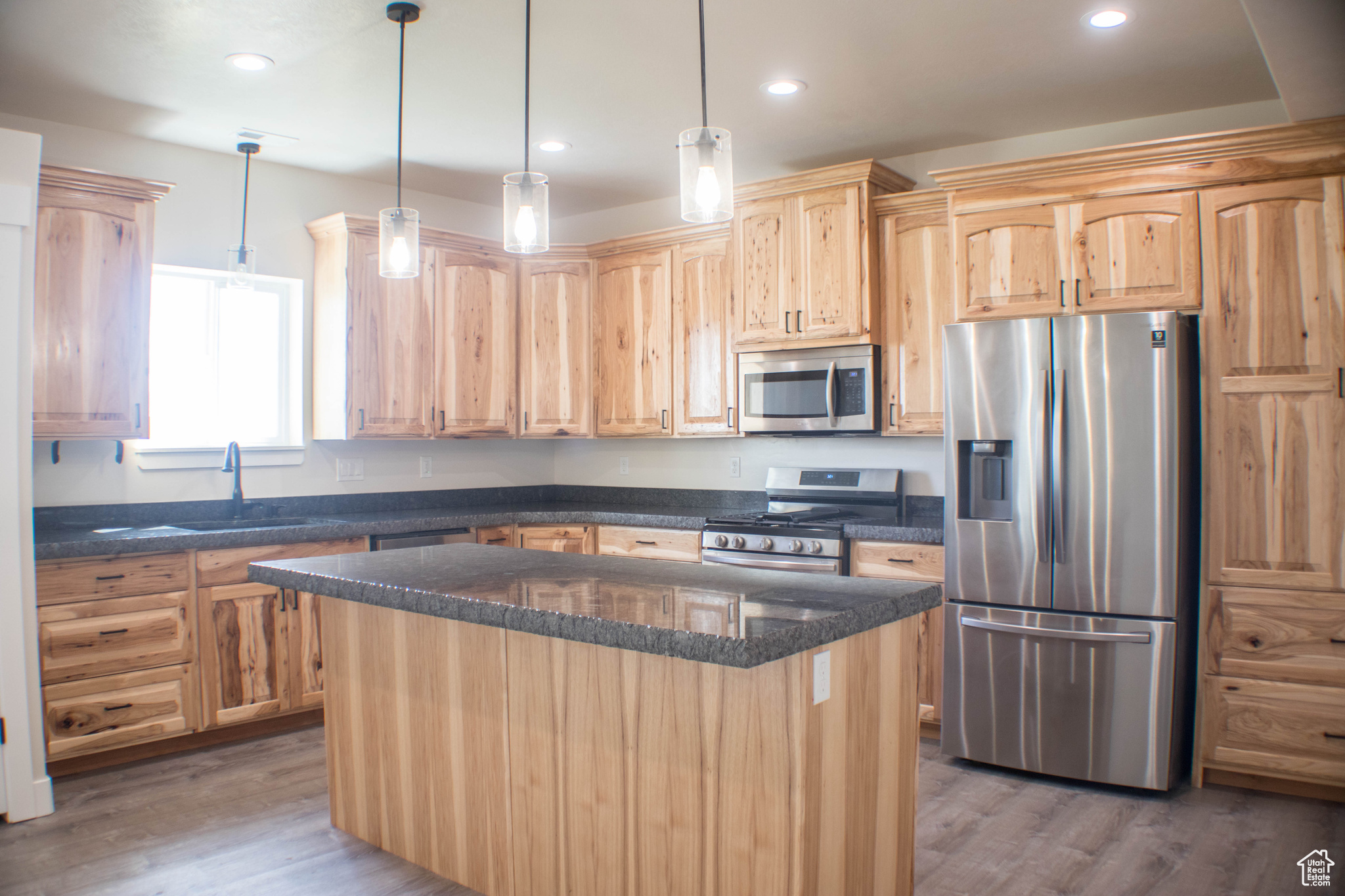Kitchen featuring appliances with stainless steel finishes, a center island, sink, hardwood / wood-style floors, and hanging light fixtures