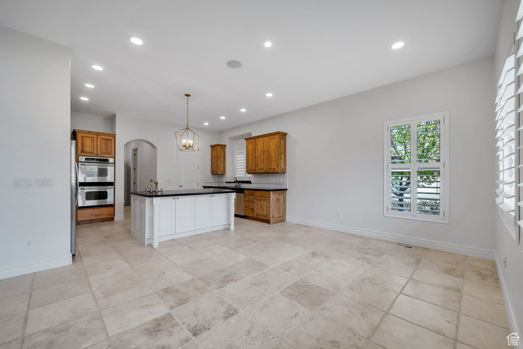 Kitchen featuring light tile floors, a kitchen island, tasteful backsplash, decorative light fixtures, and stainless steel double oven