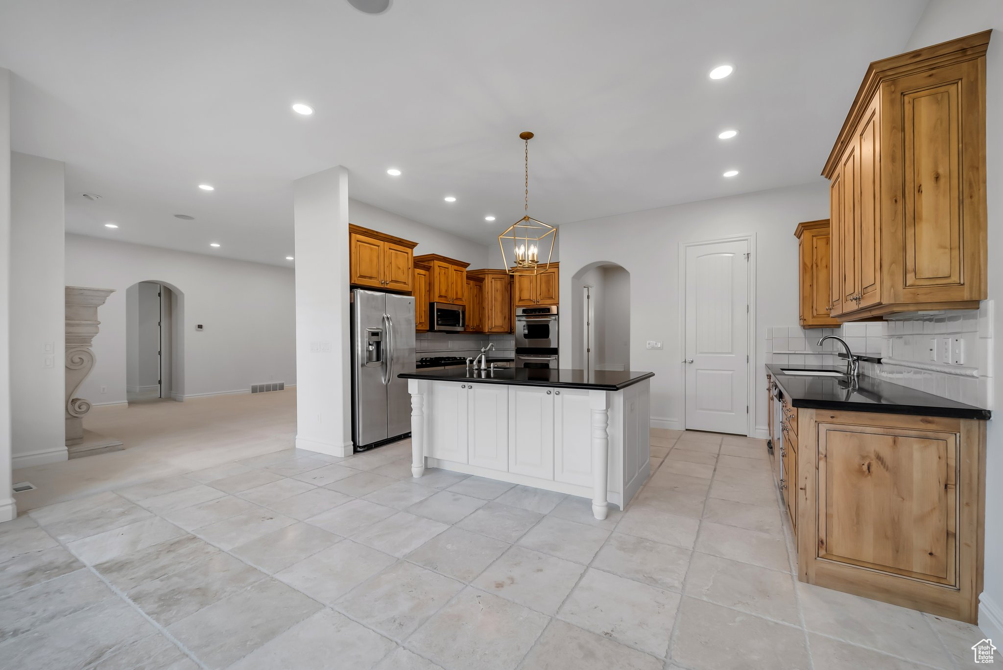 Kitchen with backsplash, stainless steel appliances, a center island with sink, sink, and light tile floors