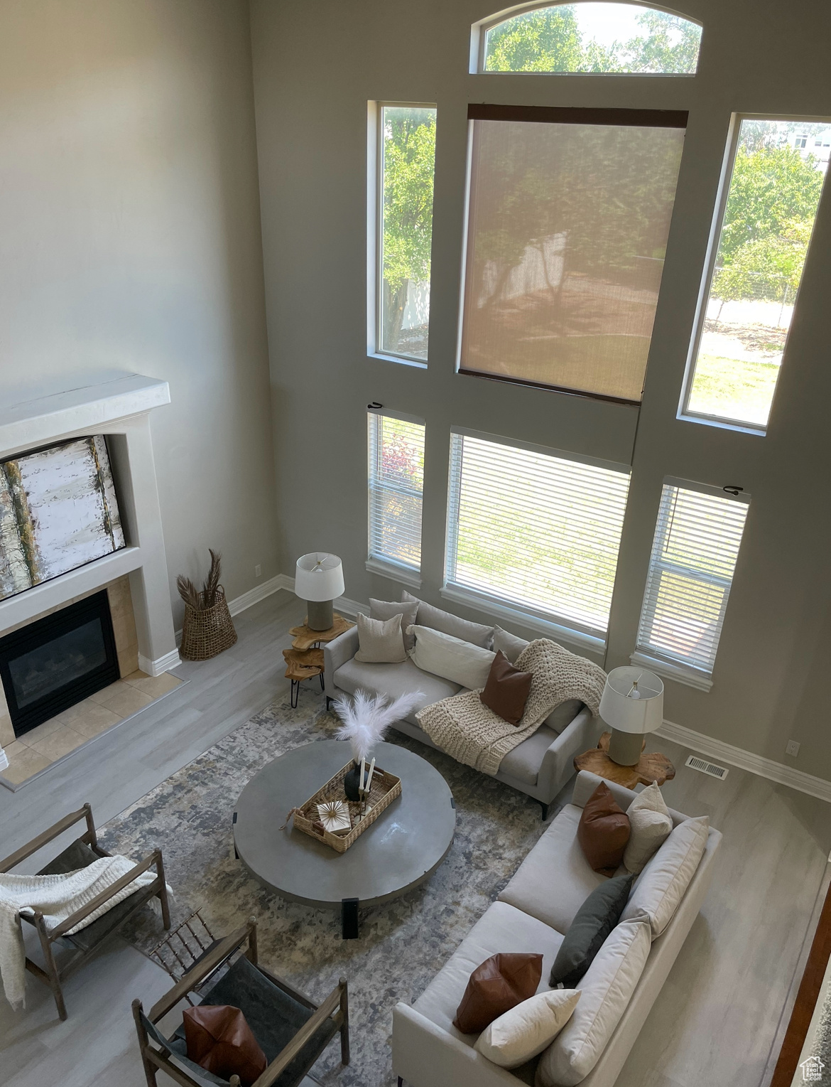 Living room with a high ceiling, a tiled fireplace, wood-type flooring, and a wealth of natural light