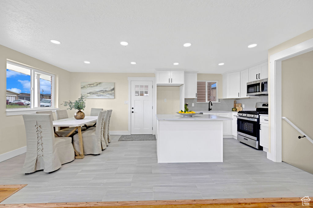 Kitchen with white cabinetry, stainless steel appliances, sink, a kitchen island, and tasteful backsplash