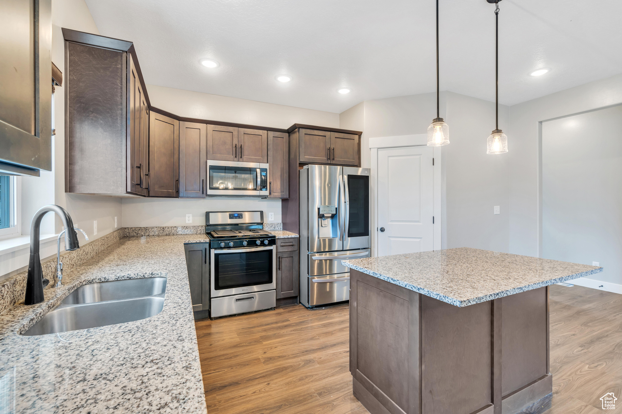 Kitchen featuring appliances with stainless steel finishes, sink, light hardwood / wood-style floors, hanging light fixtures, and light stone countertops