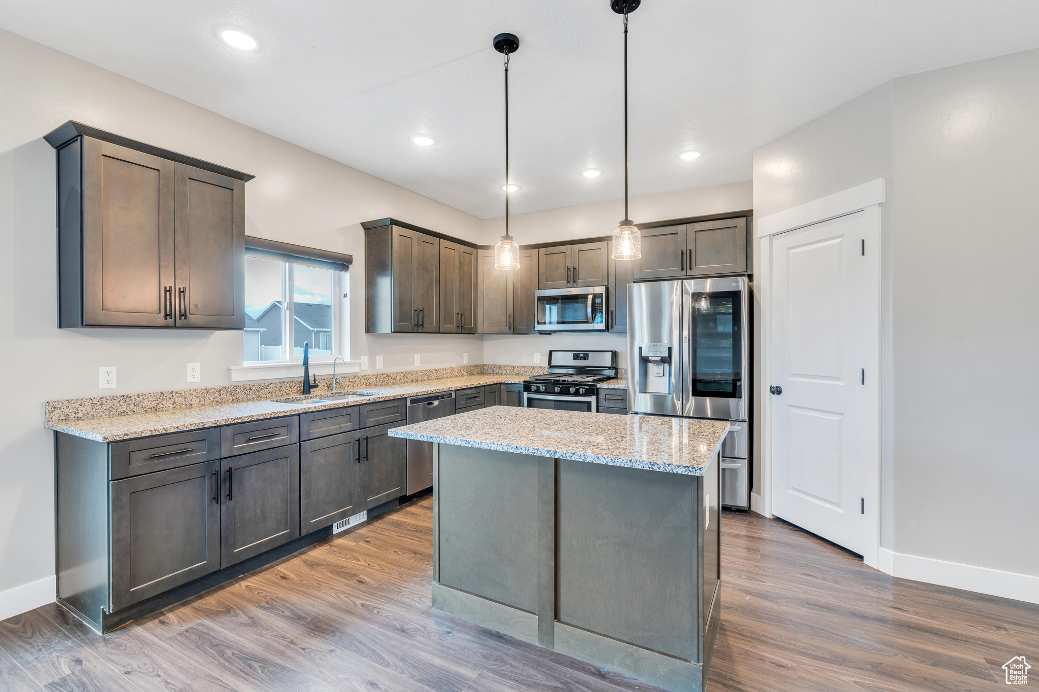 Kitchen featuring decorative light fixtures, appliances with stainless steel finishes, a center island, and hardwood / wood-style flooring