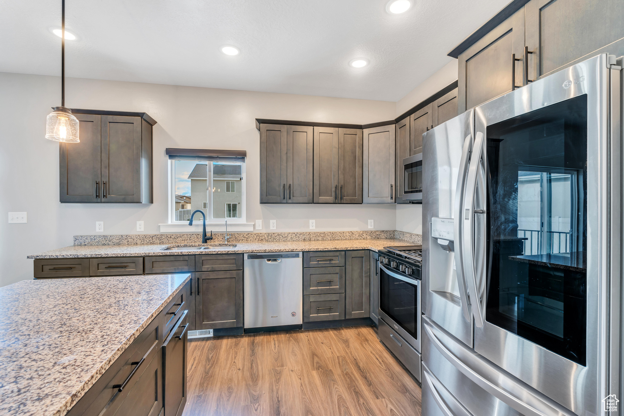 Kitchen featuring stainless steel appliances, light hardwood / wood-style floors, light stone counters, sink, and pendant lighting