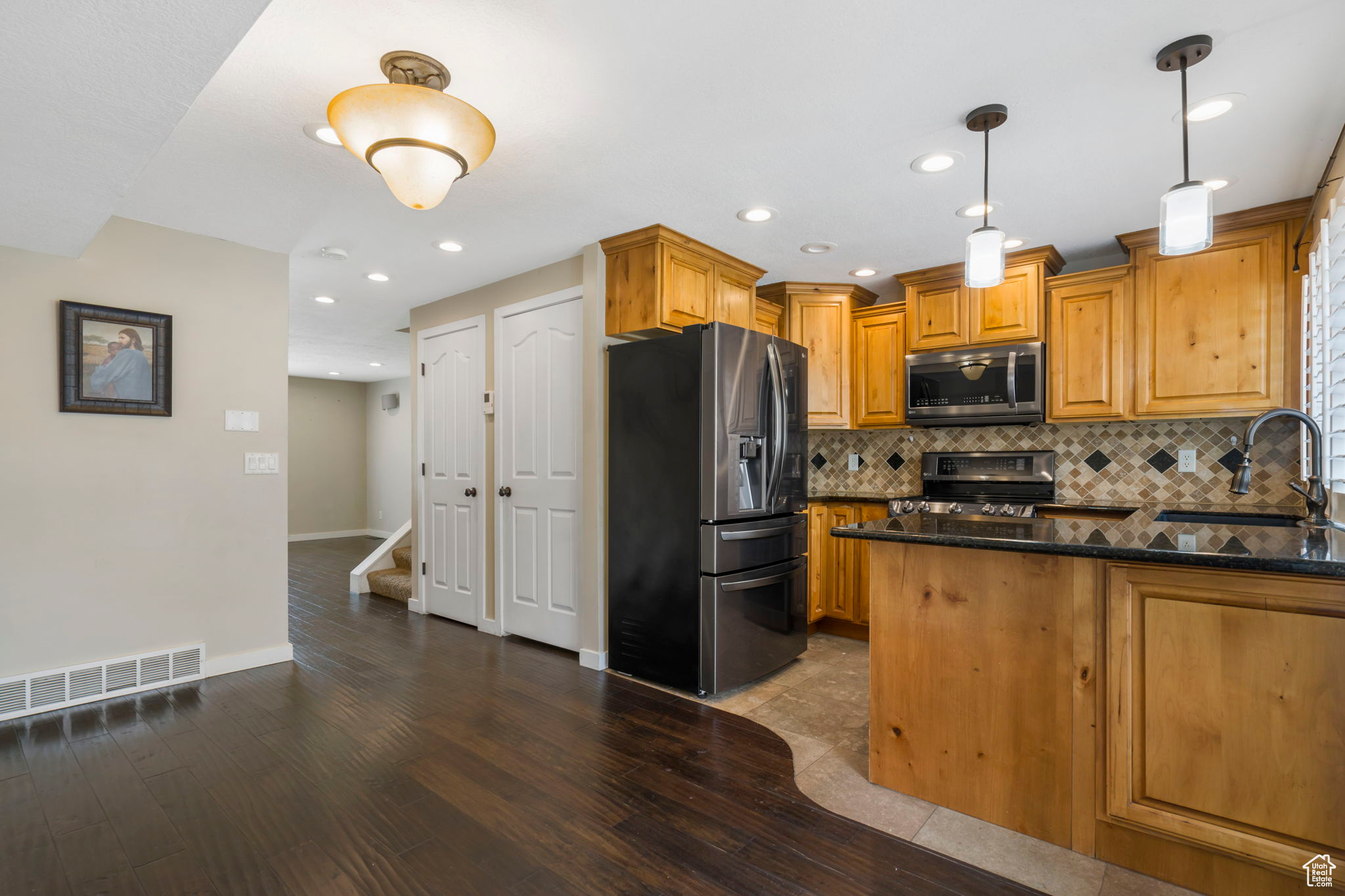 Kitchen with wood-type flooring, decorative light fixtures, backsplash, stainless steel appliances, and sink