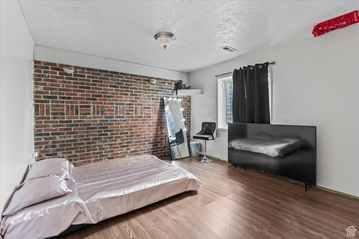 Bedroom featuring brick wall, a textured ceiling, and hardwood / wood-style floors