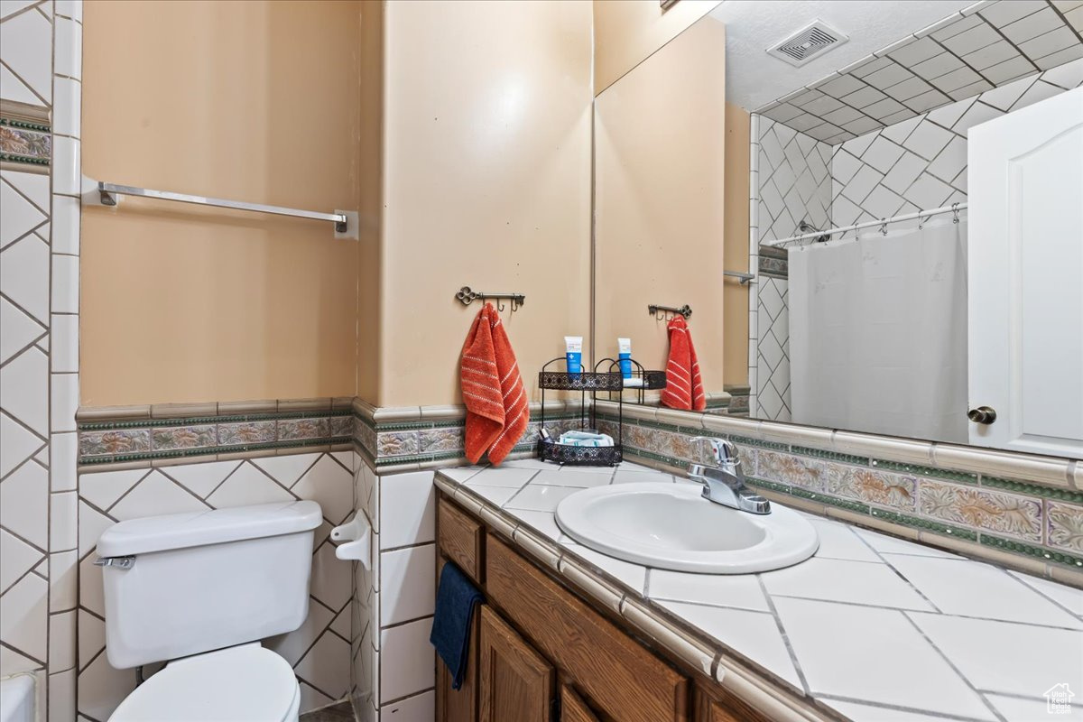 Bathroom featuring vanity, backsplash, toilet, and tile walls