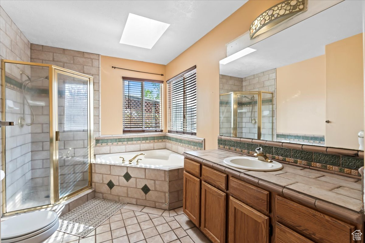 Full bathroom featuring tile floors, vanity, separate shower and tub, a skylight, and toilet