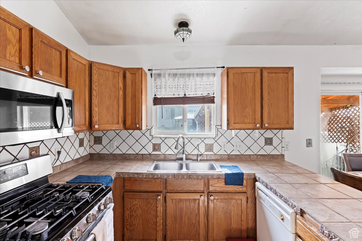 Kitchen featuring appliances with stainless steel finishes, backsplash, lofted ceiling, tile countertops, and sink