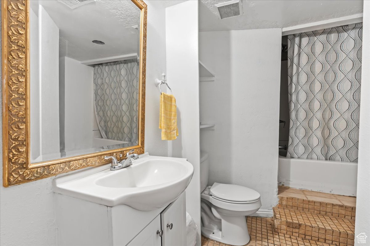 Full bathroom featuring shower / tub combo with curtain, oversized vanity, tile floors, and toilet