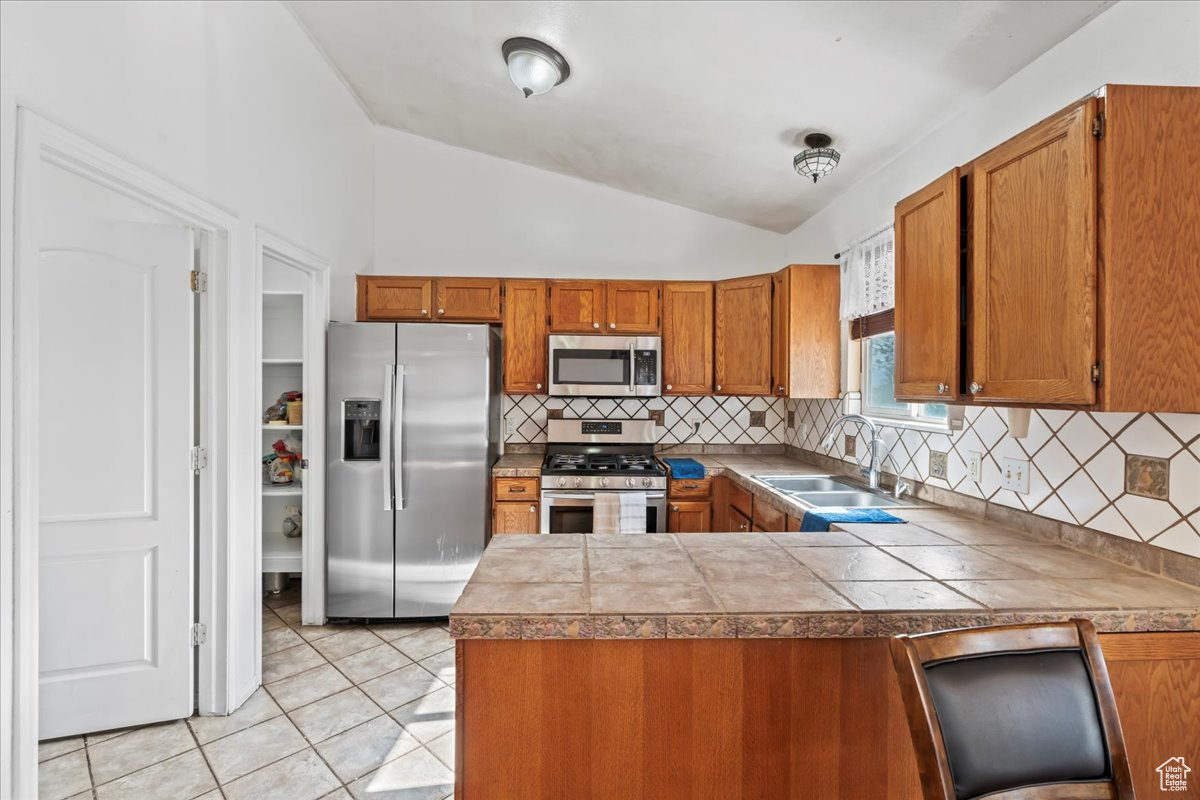 Kitchen with appliances with stainless steel finishes, sink, light tile floors, vaulted ceiling, and tasteful backsplash
