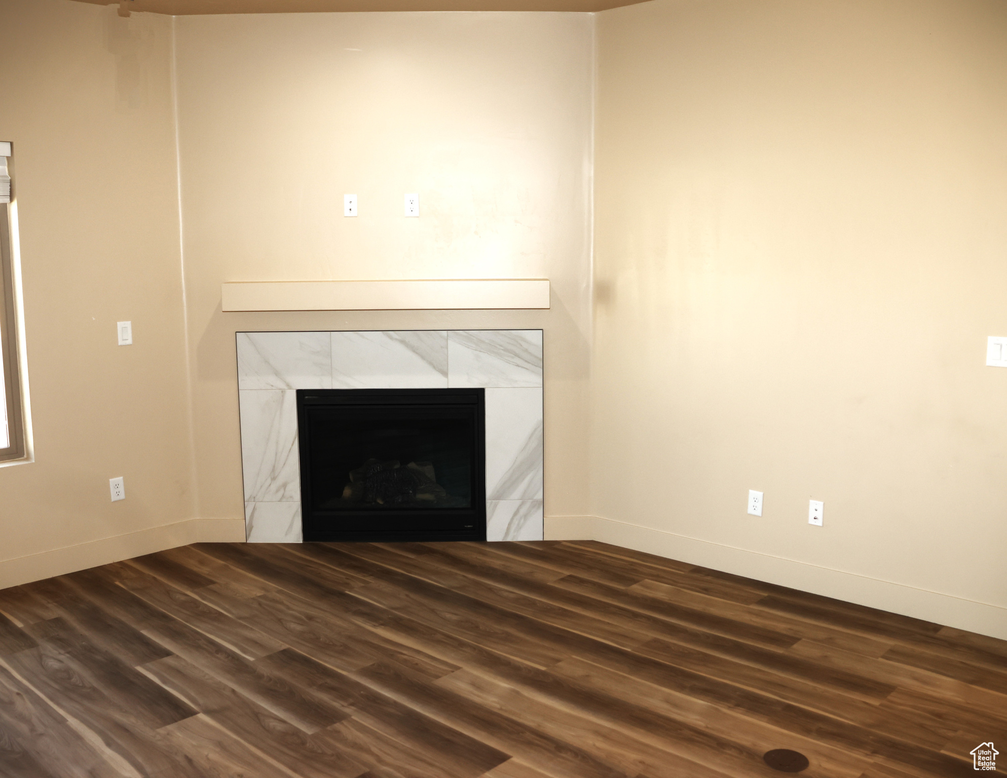 Unfurnished living room with dark wood-type flooring and a tiled fireplace