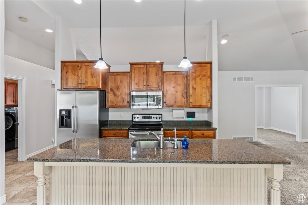 Kitchen with light colored carpet, appliances with stainless steel finishes, pendant lighting, and washer / dryer