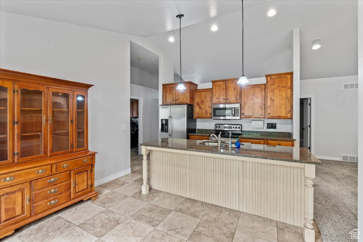 Kitchen featuring light carpet, pendant lighting, stainless steel appliances, and high vaulted ceiling