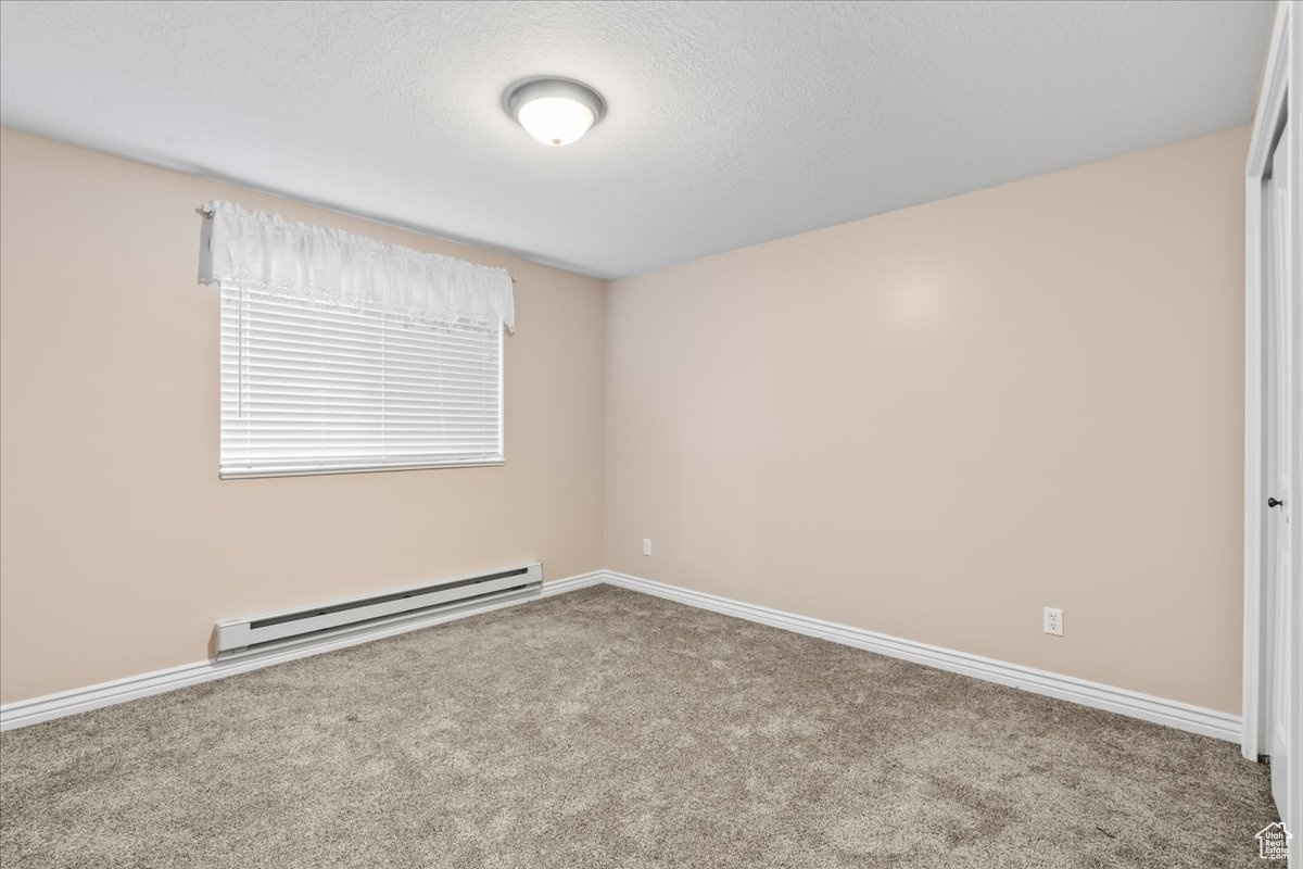 Carpeted empty room featuring a baseboard heating unit