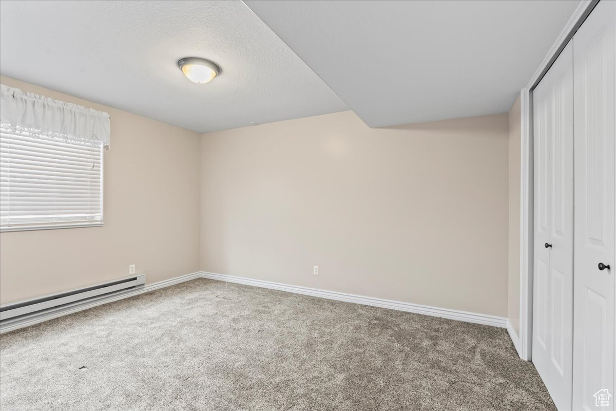 Unfurnished bedroom featuring a closet, baseboard heating, and carpet floors