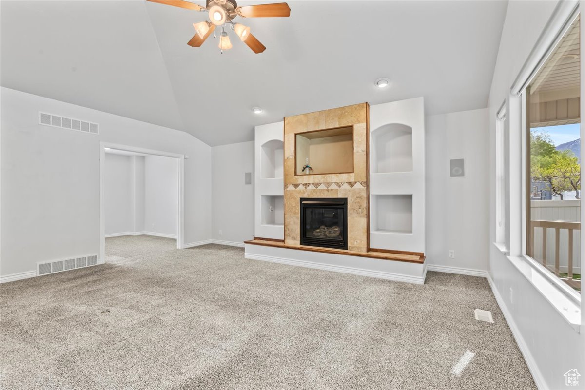 Unfurnished living room with built in shelves, carpet, vaulted ceiling, and a fireplace