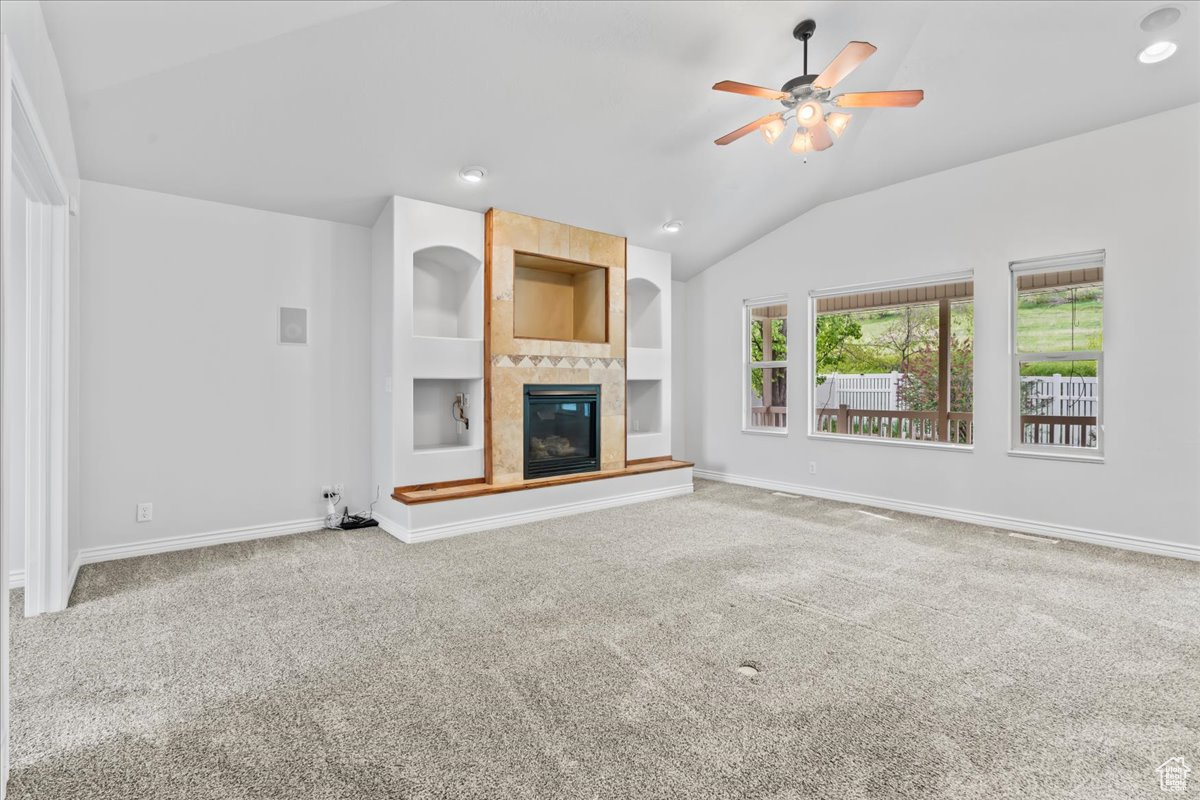 Unfurnished living room featuring carpet, a fireplace, built in features, ceiling fan, and lofted ceiling