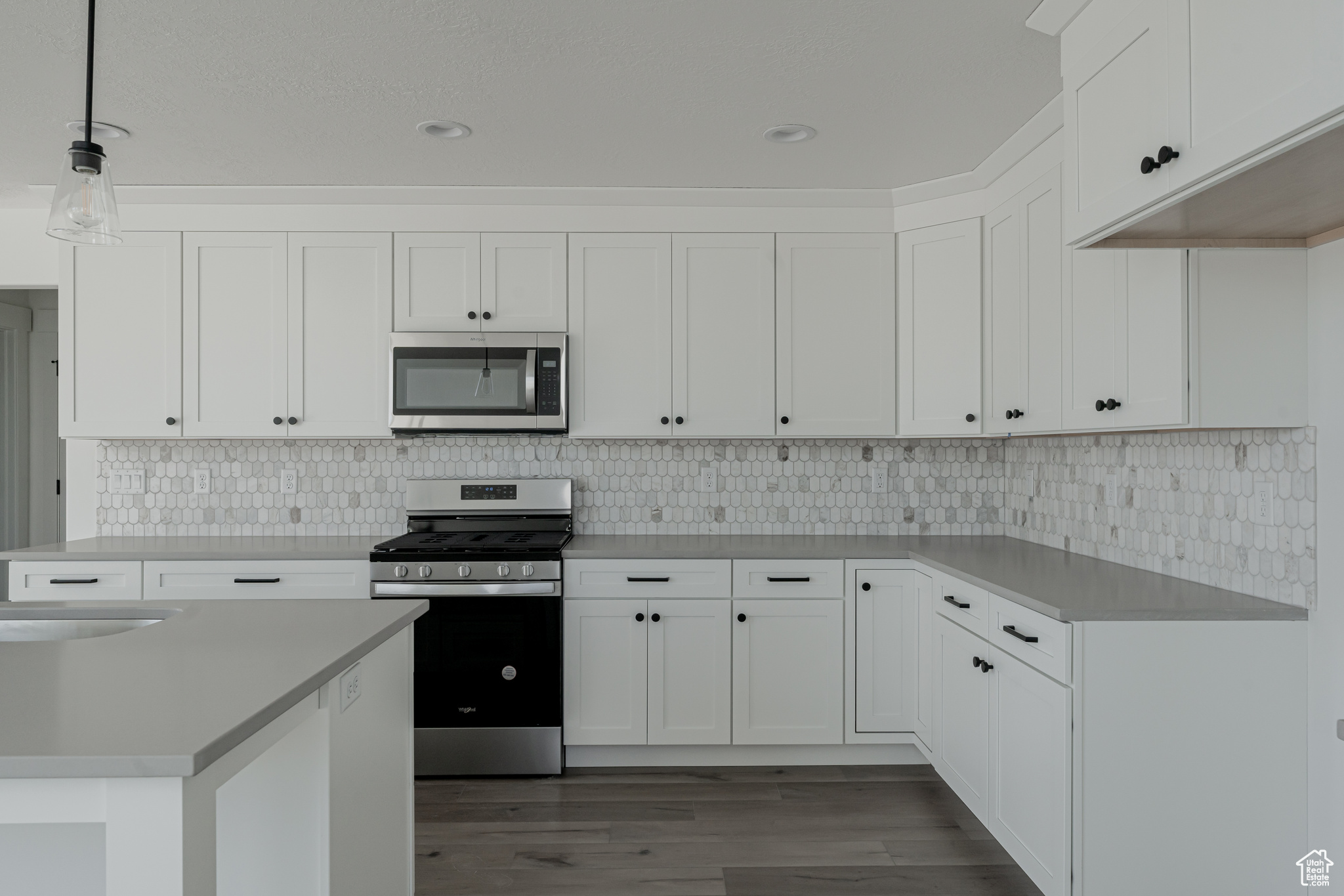 Kitchen with pendant lighting, backsplash, wood-type flooring, stainless steel appliances, and white cabinetry