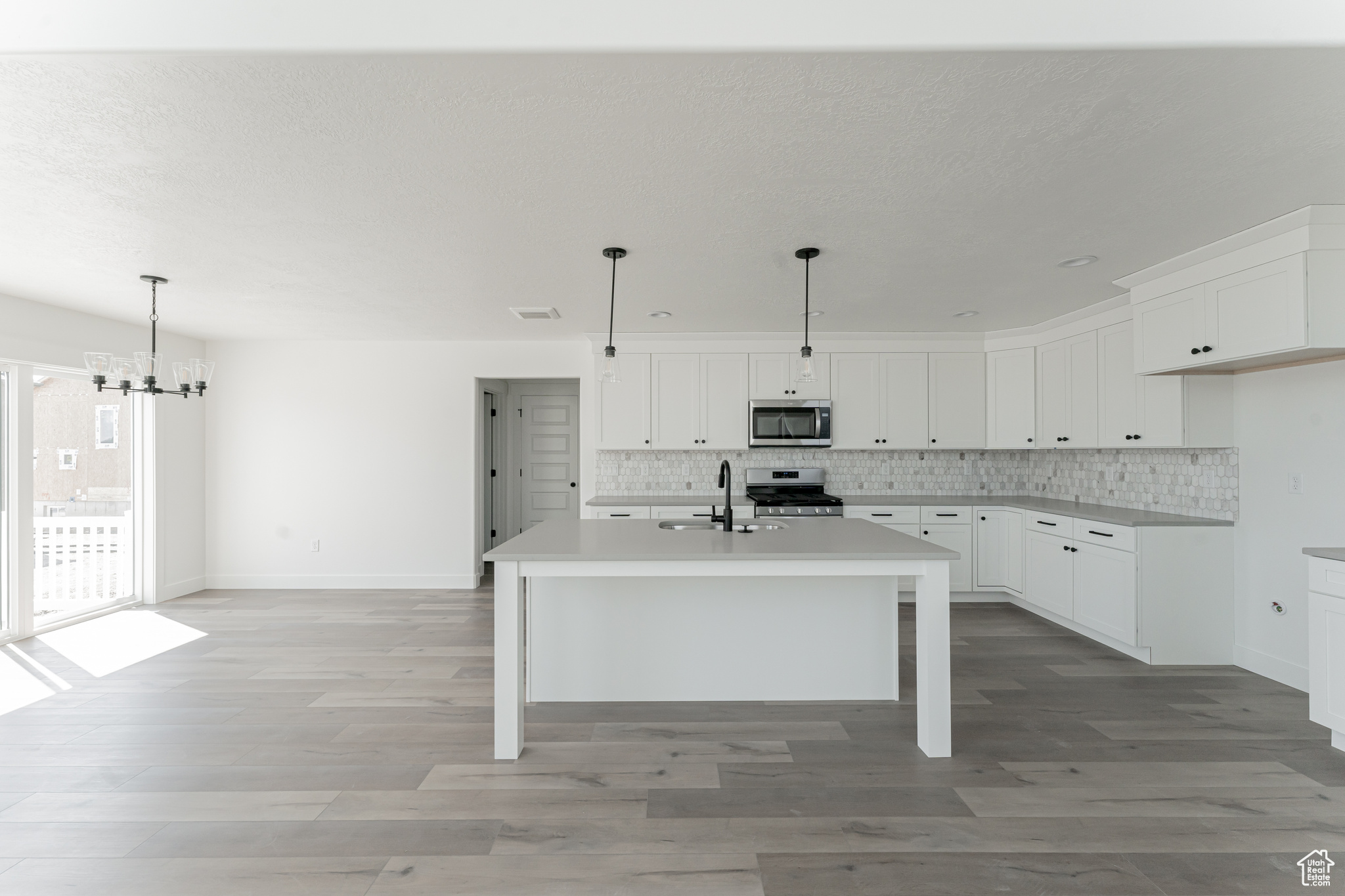 Kitchen featuring a center island with sink, appliances with stainless steel finishes, tasteful backsplash, white cabinetry, and light wood-type flooring