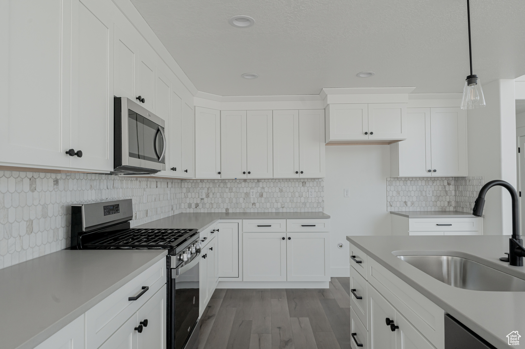 Kitchen with white cabinets, decorative light fixtures, light wood-type flooring, stainless steel appliances, and sink