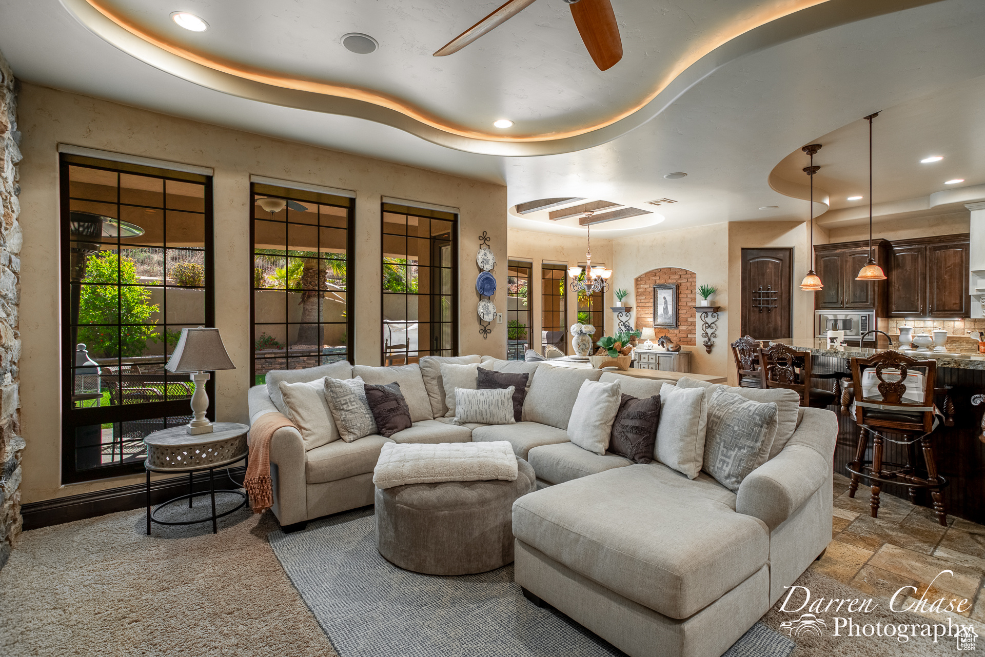 Tiled living room with ceiling fan with notable chandelier and a tray ceiling