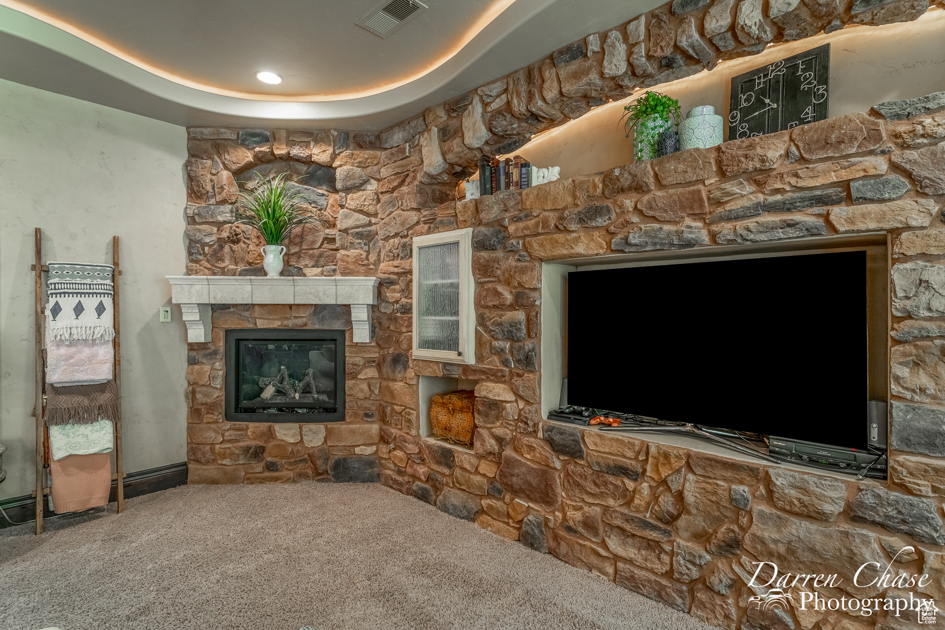 Living room with carpet flooring, a stone fireplace, and a tray ceiling