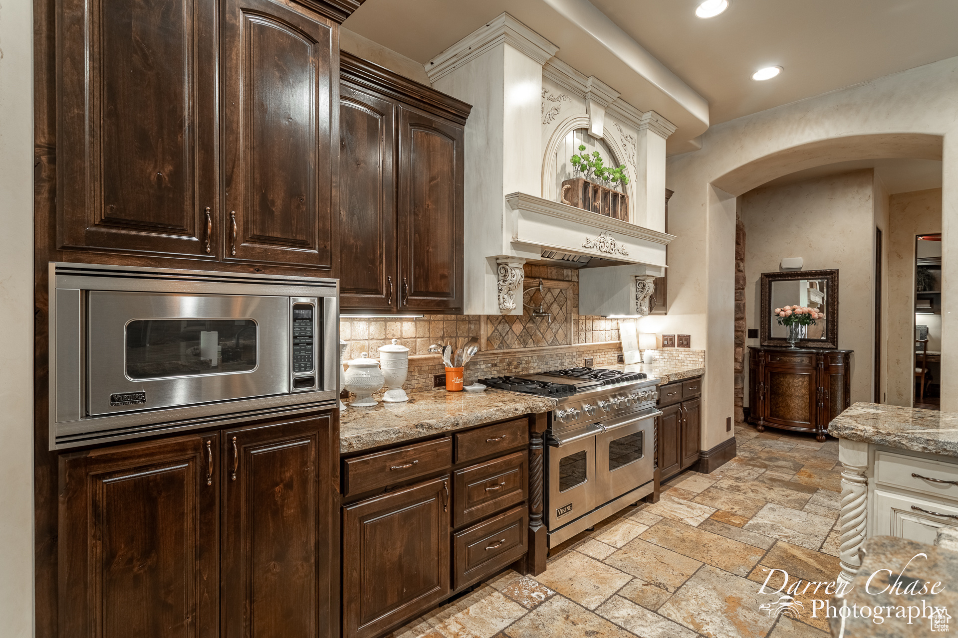 Kitchen featuring dark brown cabinets, appliances with stainless steel finishes, backsplash, light stone counters, and light tile floors