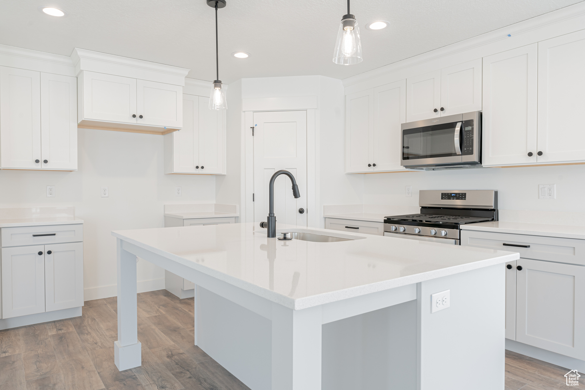 Kitchen featuring decorative light fixtures, white cabinets, an island with sink, light hardwood / wood-style floors, and appliances with stainless steel finishes