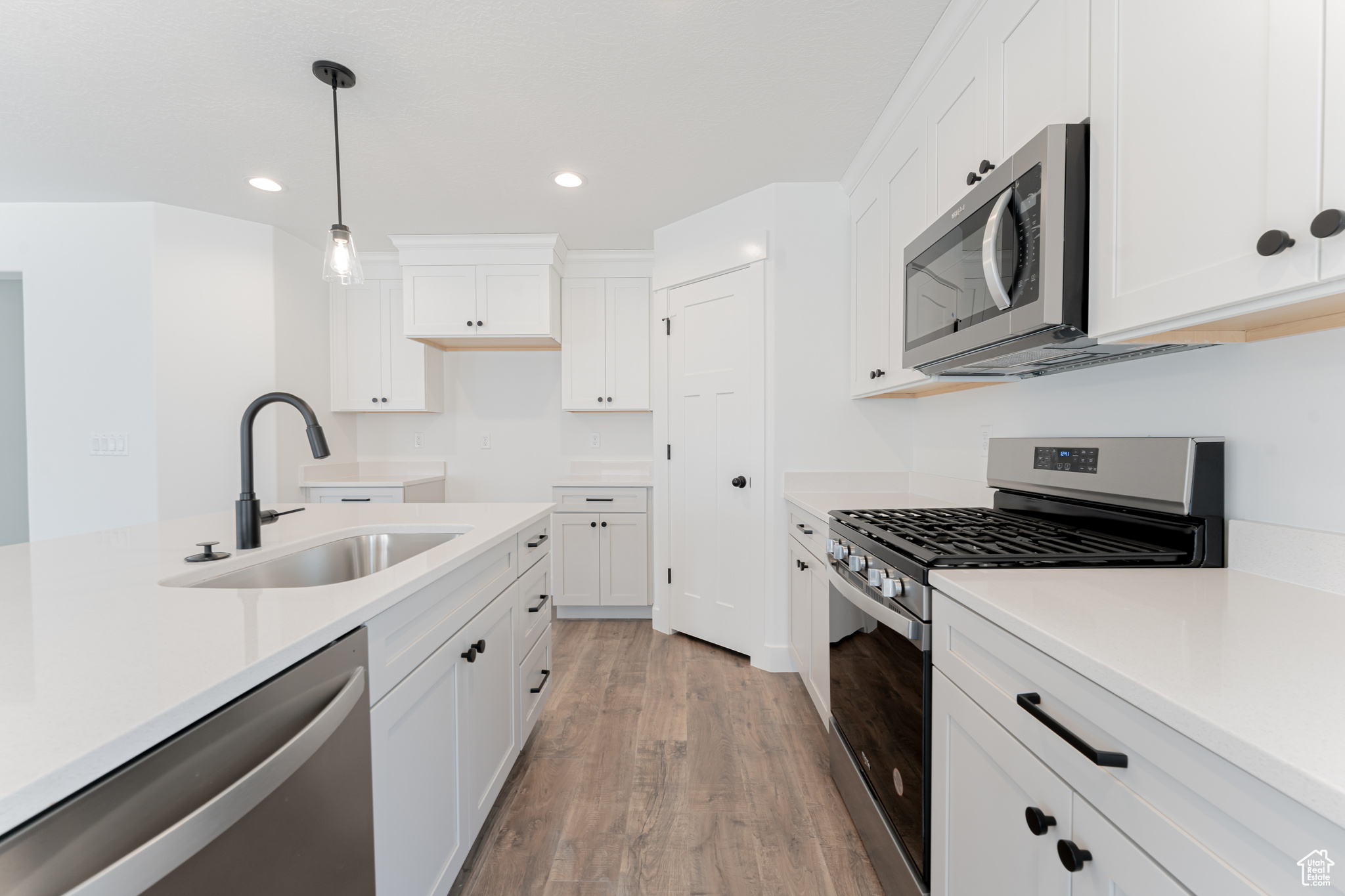 Kitchen with appliances with stainless steel finishes, light hardwood / wood-style flooring, sink, decorative light fixtures, and white cabinetry