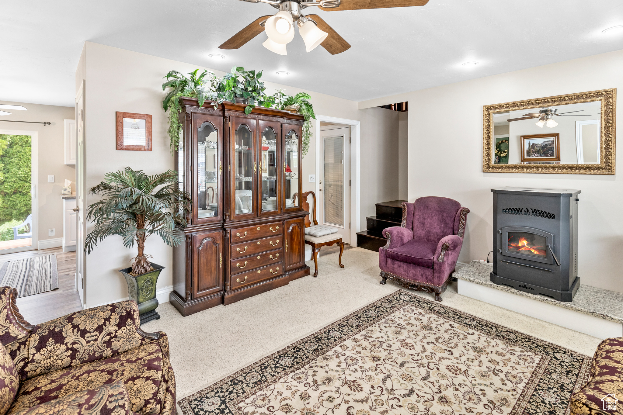 Carpeted living room featuring a wood stove and ceiling fan
