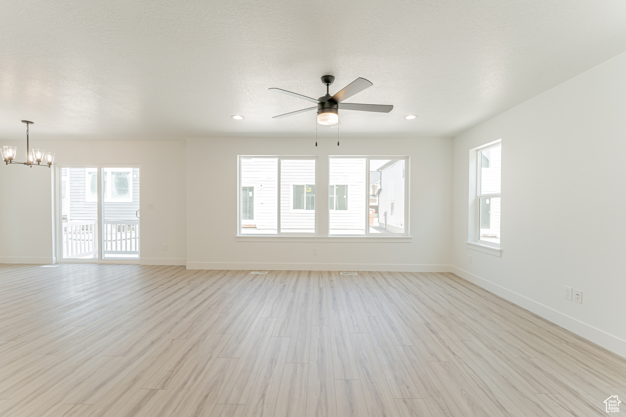 Spare room featuring ceiling fan with notable chandelier and light wood-type flooring