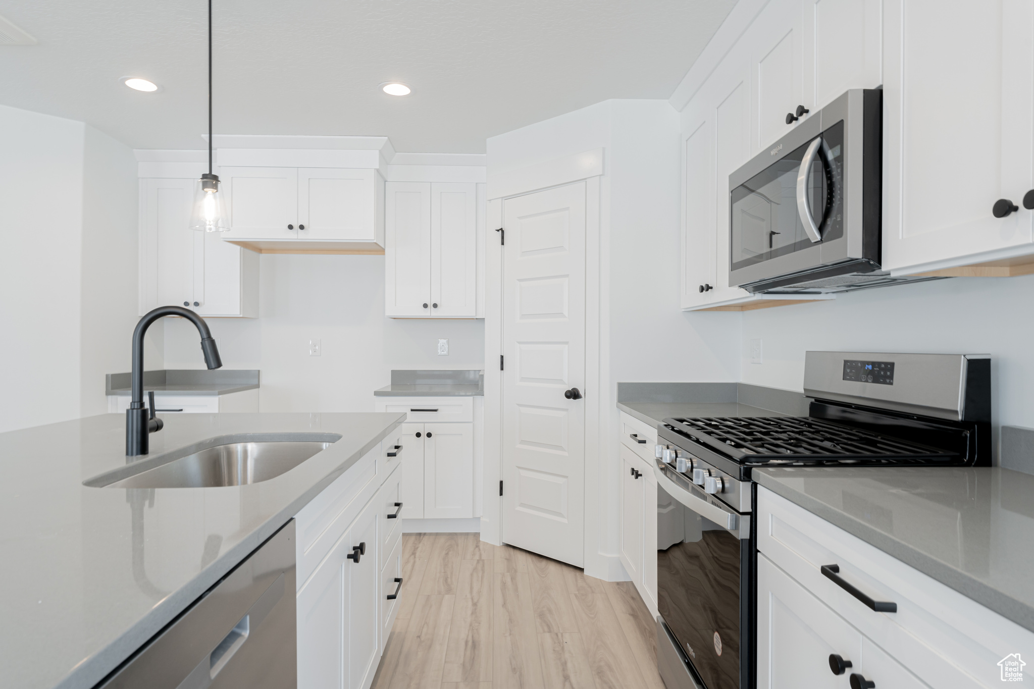 Kitchen with white cabinetry, pendant lighting, sink, light hardwood / wood-style floors, and appliances with stainless steel finishes