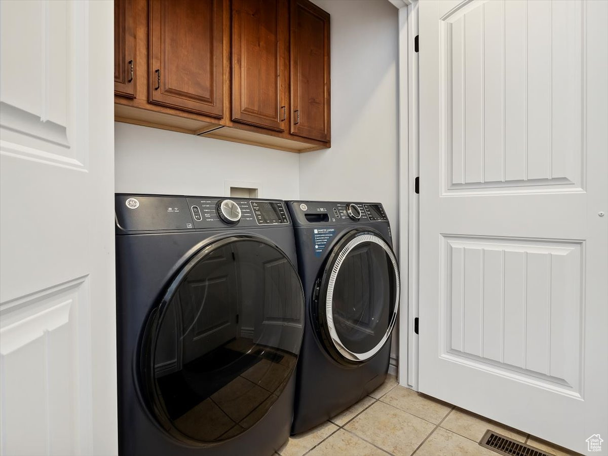 Laundry room with washing machine and dryer, cabinets, and light tile flooring
