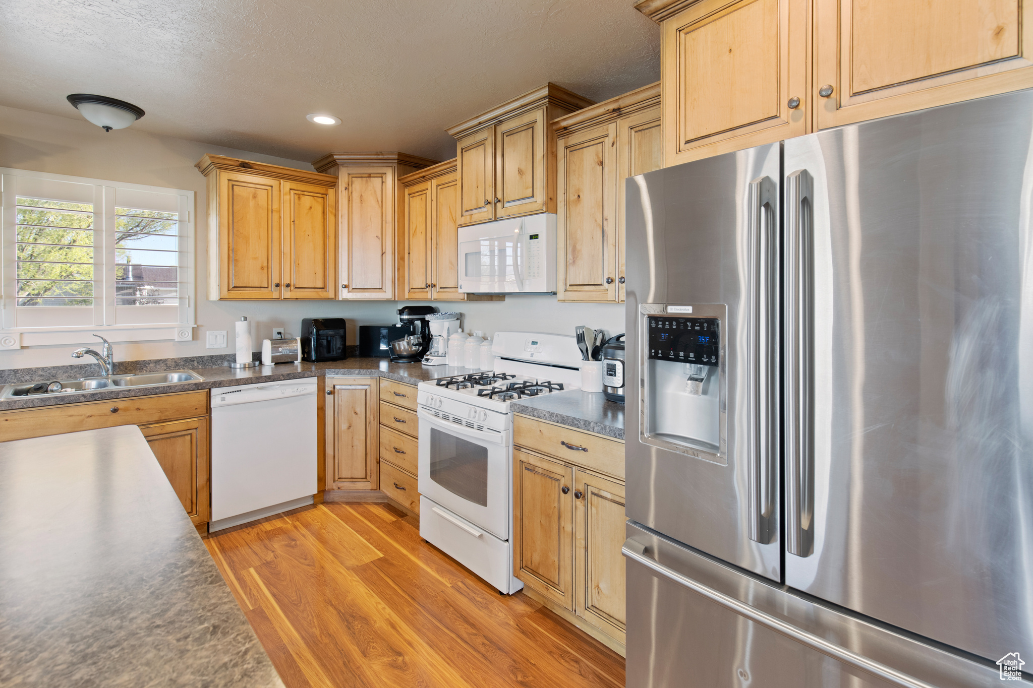 Kitchen with light hardwood / wood-style floors, white appliances, and sink