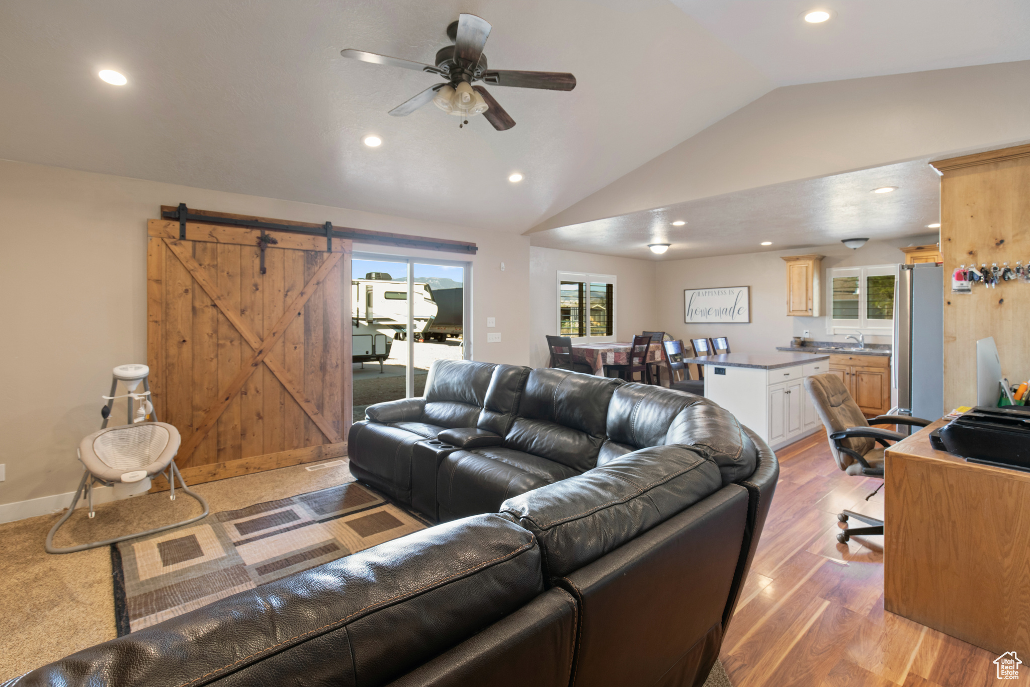 Living room featuring light wood-type flooring, a barn door, sink, vaulted ceiling, and ceiling fan