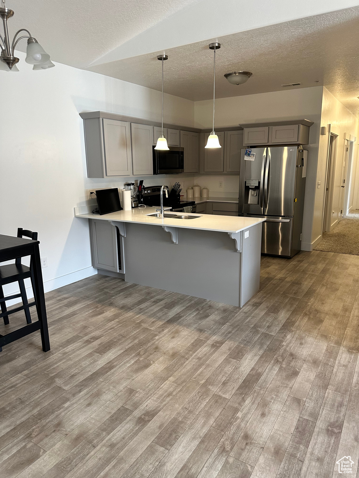 Kitchen with pendant lighting, kitchen peninsula, stainless steel appliances, a breakfast bar area, and hardwood / wood-style flooring