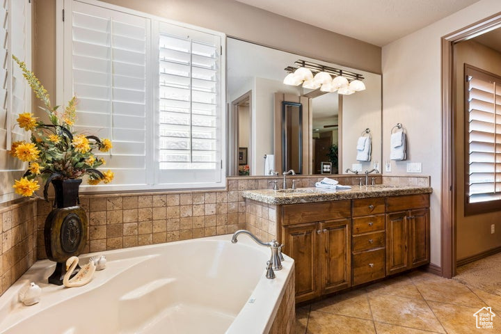 Bathroom featuring a wealth of natural light, dual bowl vanity, tile flooring, and a washtub