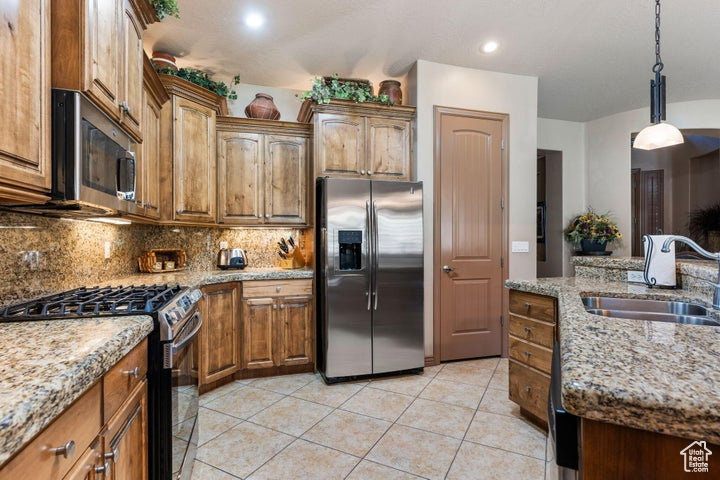 Kitchen with light tile floors, sink, hanging light fixtures, stainless steel appliances, and light stone countertops