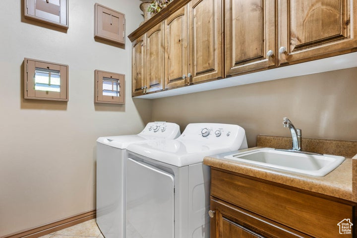 Washroom featuring light tile floors, washing machine and clothes dryer, cabinets, and sink