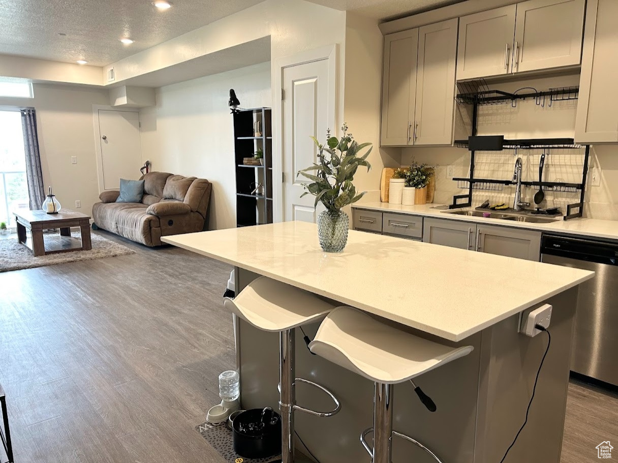 Kitchen featuring sink, tasteful backsplash, gray cabinetry, stainless steel dishwasher, and light hardwood / wood-style flooring