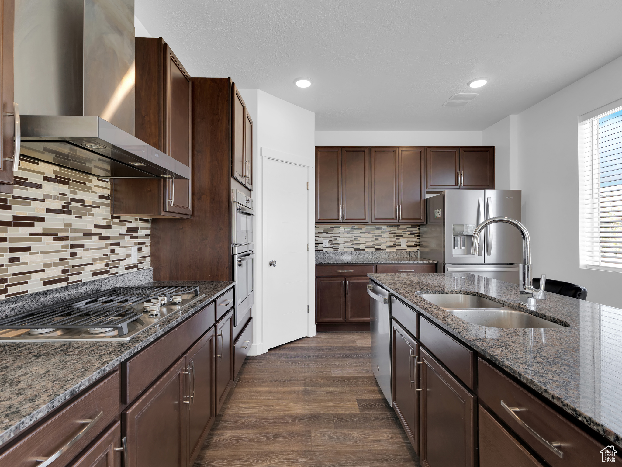 Kitchen featuring wall chimney exhaust hood, dark hardwood / wood-style floors, appliances with stainless steel finishes, sink, and tasteful backsplash
