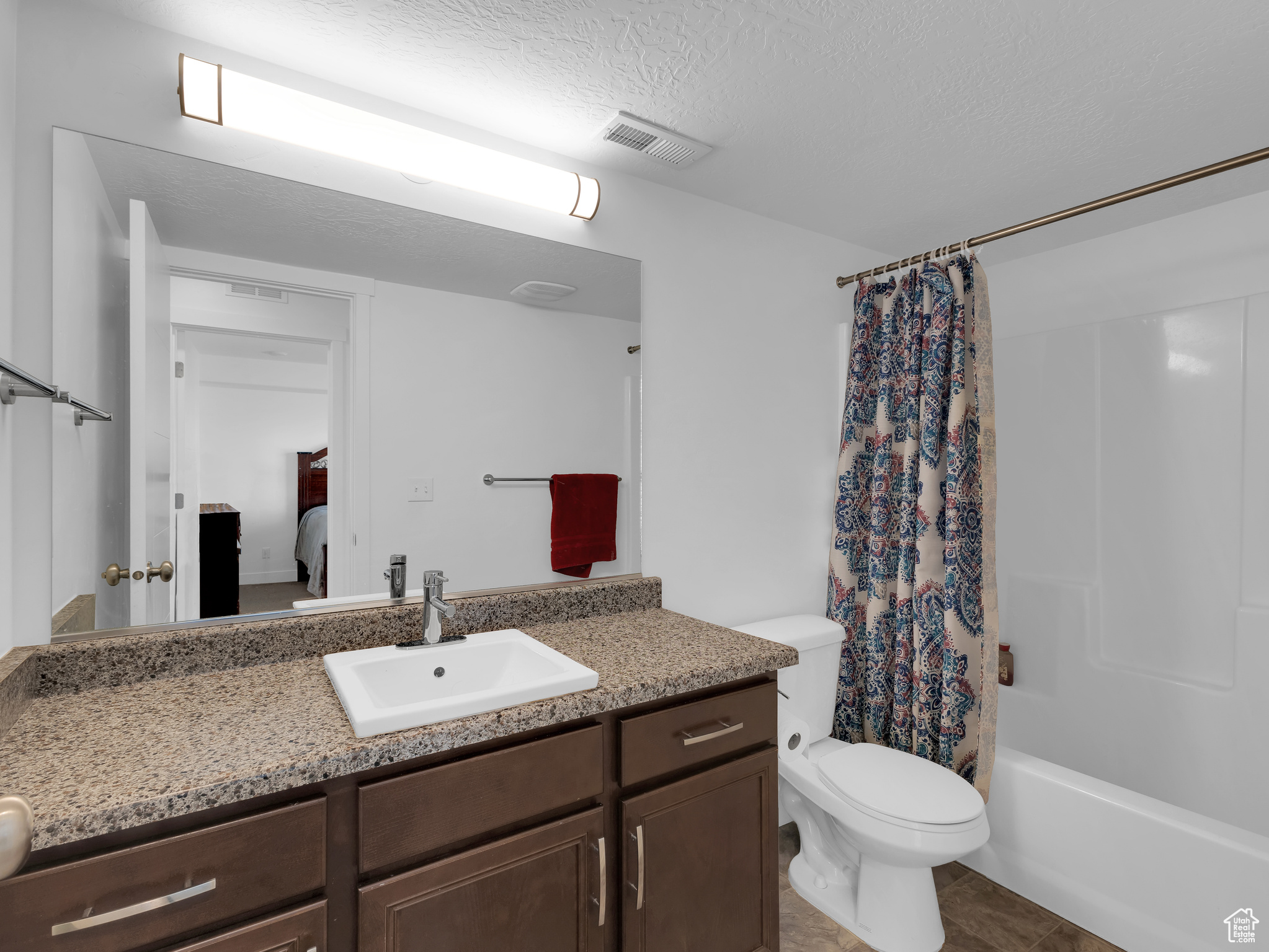 Full bathroom featuring shower / bath combo with shower curtain, a textured ceiling, oversized vanity, tile floors, and toilet